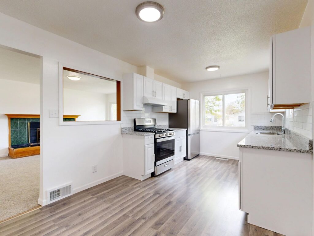 Bright, newly renovated kitchen featuring white cabinets, hardwood floors, and stainless steel appliances.